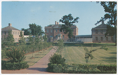 The Palace is red brick with a large court yard field with trees, plants and flowers. 