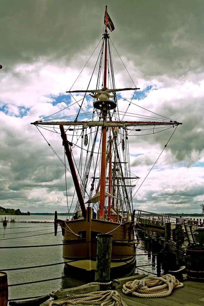 Sailing ship in Jamestown Sailing ship in Jamestown. It is docked in a harbor. It is clad with several masts and ropes for the masts. It is a cloudy day.
