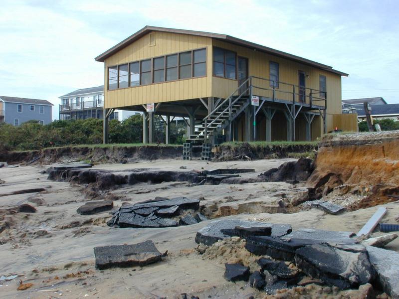 North Carolina Hurricane Floyd & Irene (DR-1292) Yellow house on a ruined beach in Oak Island after Floyd. Broken pieces of the road litter the beach. There is a blue sky in the background.