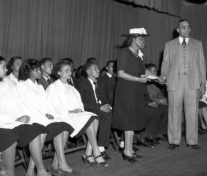 Charlotte Hawkins Brown onstage with students Charlotte Hawkins Brown on stage at Palmer institute with students. There students seated behind her and she is shaking hands with a man in a suit.