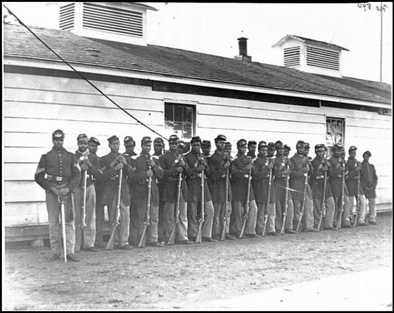 Photograph of all African-American Company E, 4th U.S. Colored Infantry, at Fort Lincoln 27 African Americans of Company E during the Civil War, standing in two lines with rifles resting on the ground.