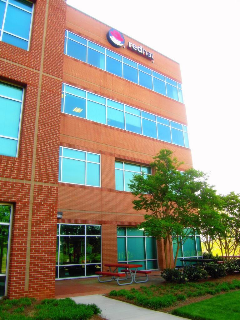 Corporate Headquarters for redhat, inc. RedHat building. It is a sunny day and there are plants in front. There is a paved sidewalk.