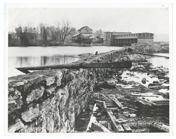 Idol’s Dam and Power Plant on the Yadkin River Idol's dam. A reservoir of water is held by a stone wall. A facility sits at the top of the reservoir next to a home. Trees surround the reservoir.