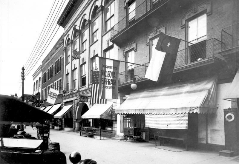Headquarters of the North Carolina Equal Suffrage Association A building with a flags hanging outside, one of which reads "North Carolina Equal Suffrage Association."